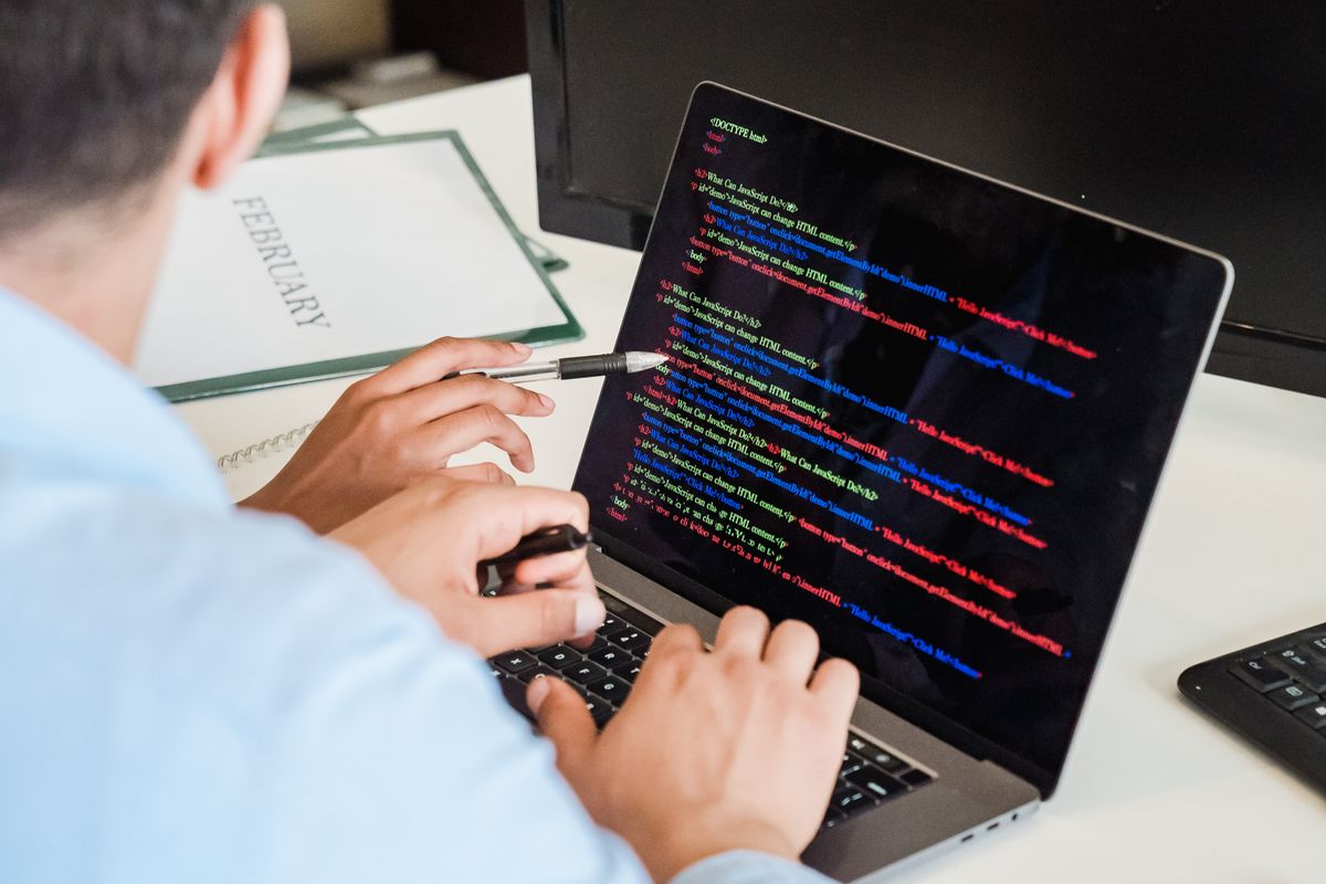A developer pointing at syntax-highlighted code on a laptop screen at a desk
