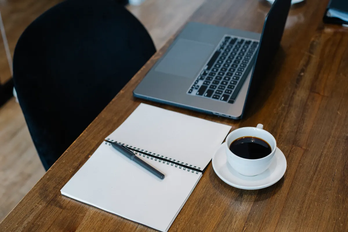 Laptop, open notebook and coffee on a wooden desk, set up to work on an Android take-home assignment