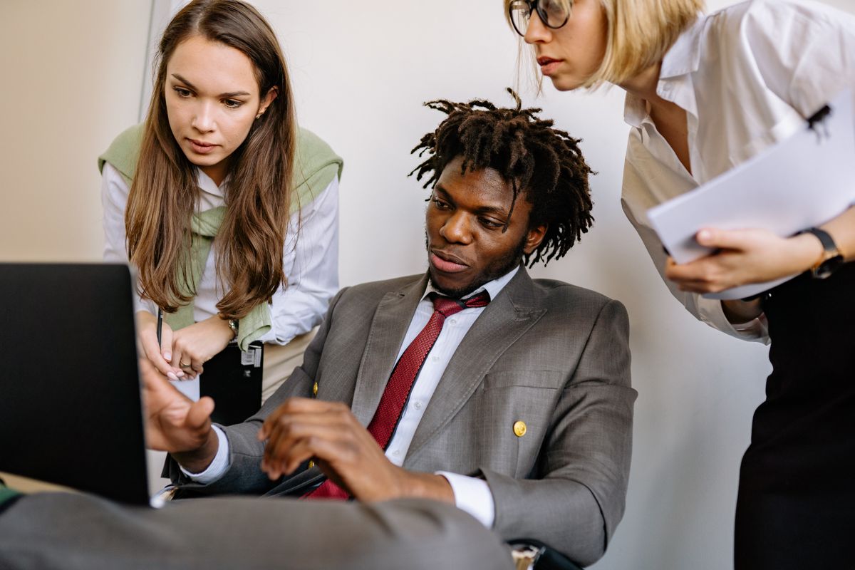 Three colleagues talking through a project in an office, the kind of cross-team working relationship behavioral interview scoring often probes