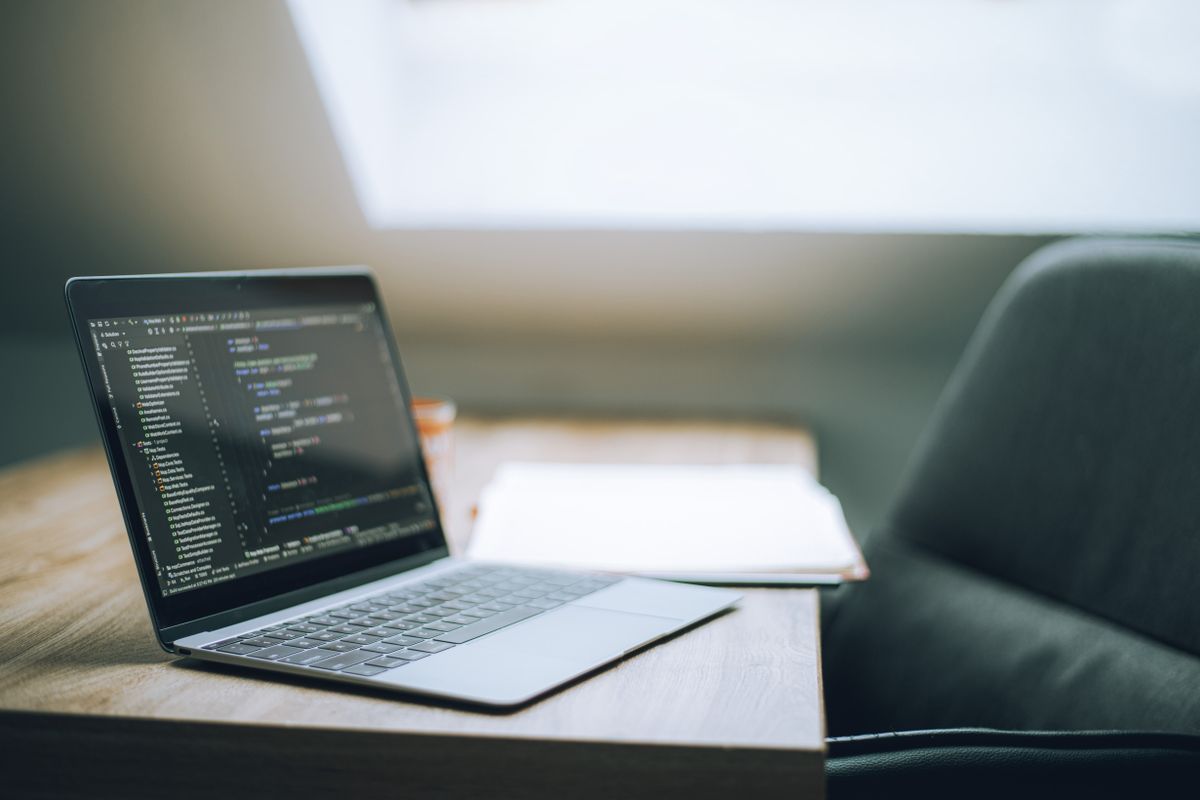 Laptop showing a dark-themed code editor on a wooden desk, representing Jetpack Compose development