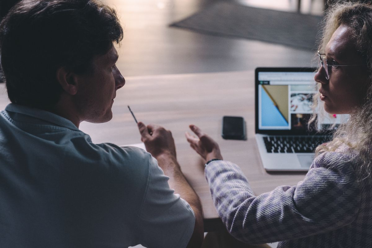 Two colleagues having a serious discussion while reviewing work on a laptop, the kind of ordinary disagreement a conflict interview question is asking about