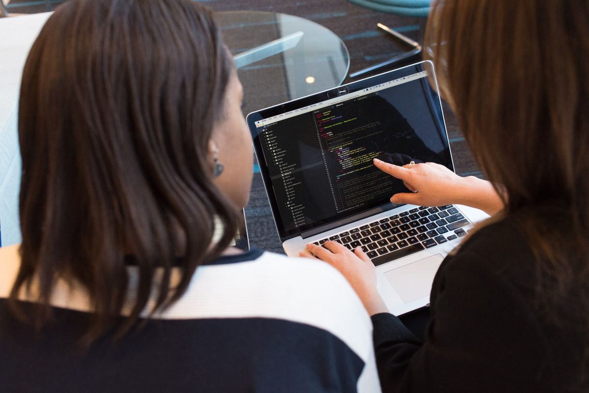 Two engineers reviewing code together, one pointing at a line on the laptop screen, illustrating critical feedback in a code review
