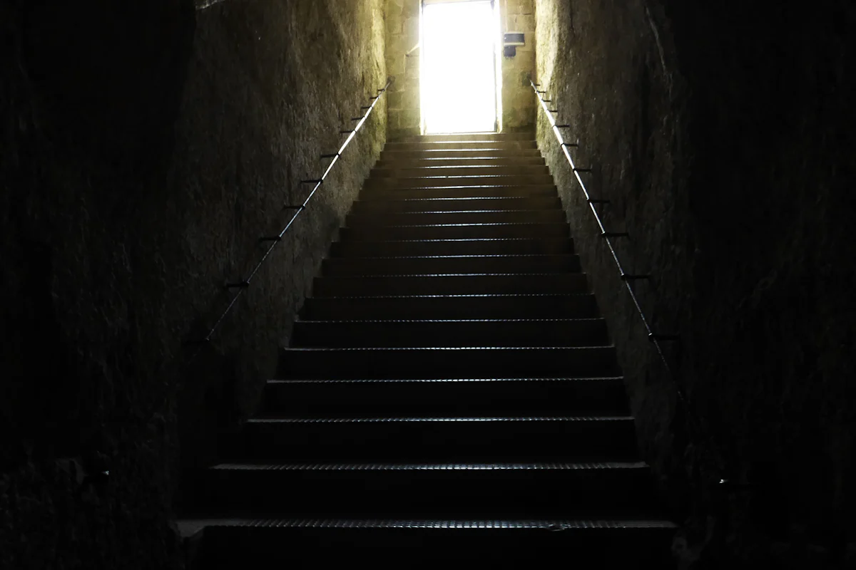 Dark stone staircase climbing toward a bright doorway, illustrating a downleveled offer one step below the target level