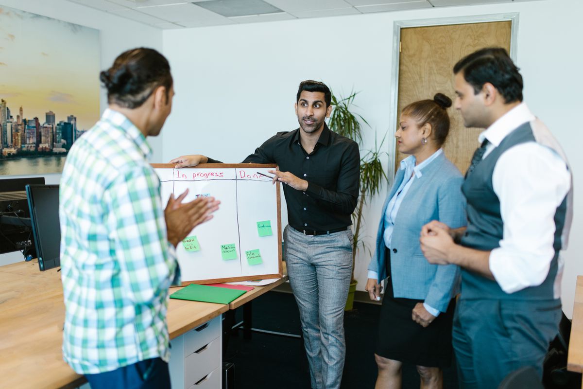 One person pointing to a specific item on a project board while colleagues listen, the kind of moment an "I" statement in a behavioral story is supposed to name