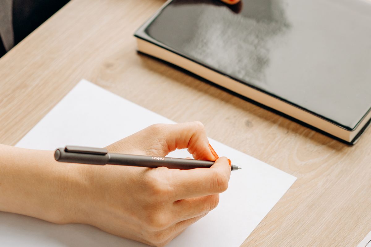 A person writing notes on paper next to a closed notebook, the kind of prep that surfaces a story's real scope before an interview