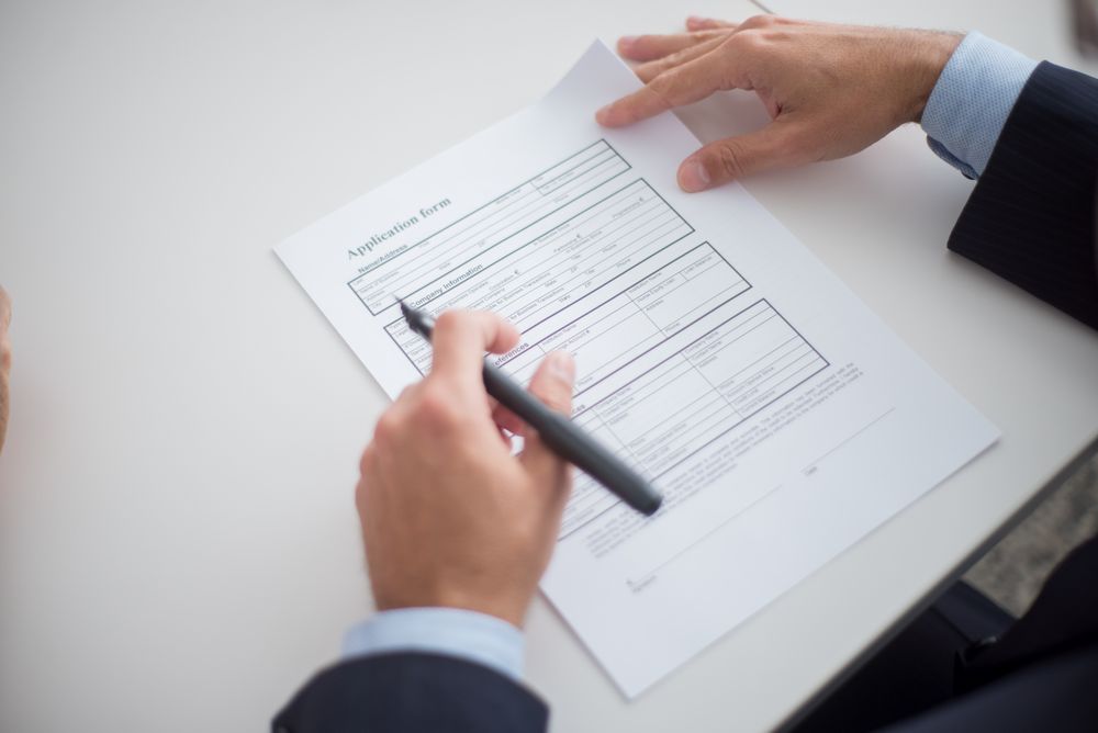 A close-up of hands writing on an application form, the kind of note that gets written about a candidate after the interview ends